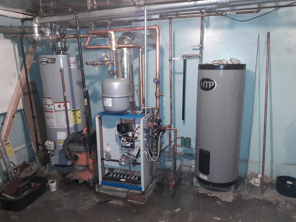 New gas boiler in a basement with new copper piping, a grey expansion tank above it, a steel flue liner, and a tall HTP indirect hot water tank on the right
